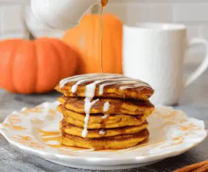 Fluffy cinnamon swirl pumpkin pancakes topped with whipped cream and maple syrup on a decorative plate, perfect for fall breakfast