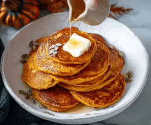 Delicious Pumpkin Ricotta Pancakes topped with maple syrup and fresh cinnamon, served on a white plate for a cozy fall breakfast.